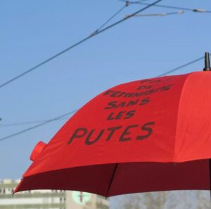Un parapluie rouge (symbole de la lutte pour les droits des travailleureuses du sexe) présente l'inscription au feutre noir "PAS DE FÉMINISME SANS LES PUTES".